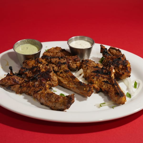 Grilled lamb chops with two dipping sauces and sliced onions on a white plate.