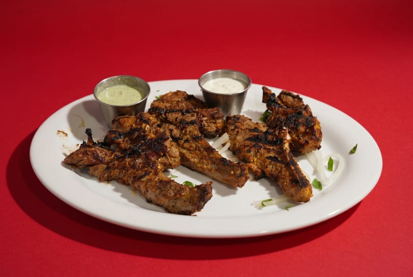 Grilled lamb chops with two dipping sauces and sliced onions on a white plate.