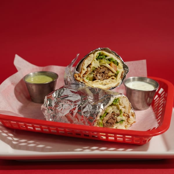 Two foil-wrapped burritos with meat and lettuce, served in a red basket with two dipping sauces.