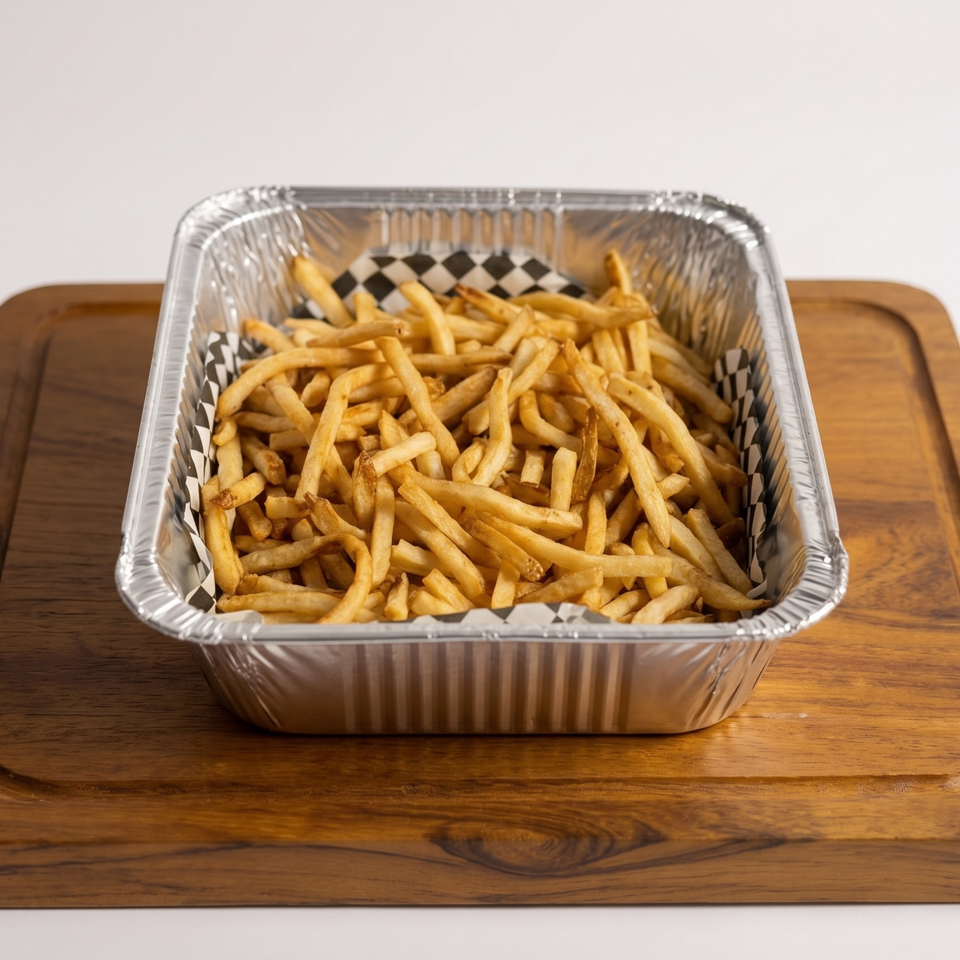 Golden french fries in a foil container with checkered paper, on a wooden cutting board.